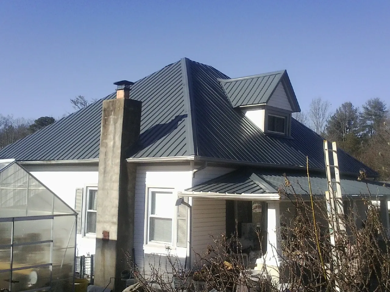Dark blue standing seam metal roof on a white farmhouse with dormer — Slate & Tile Roof Repair by Roofing Brothers in Pine Bluffs