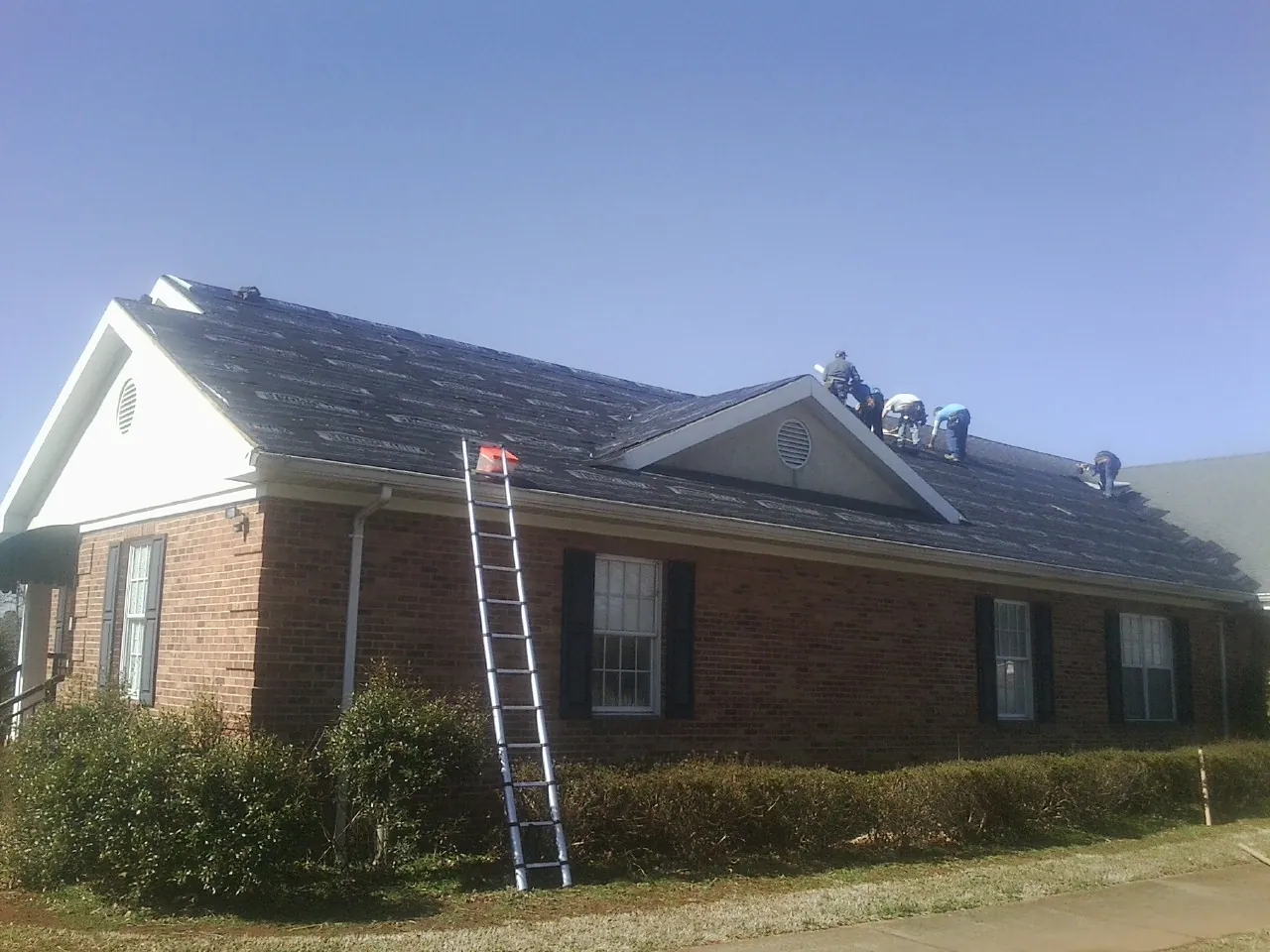 Crew tearing shingles off a brick ranch roof with a ladder set — Emergency Roof Repair work by our crew in Pine Bluffs