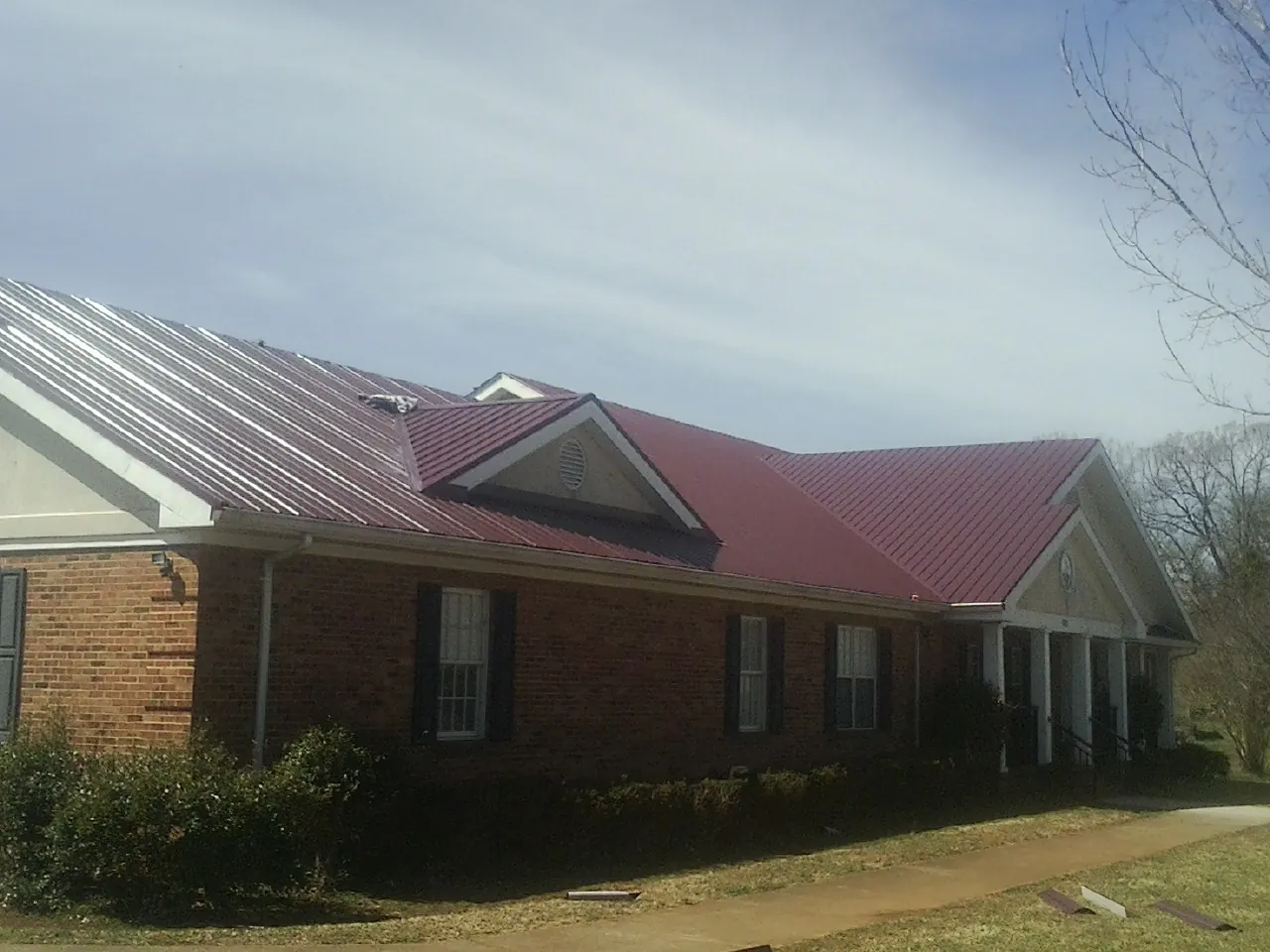 Red metal roof with gabled entries on a long brick building, from a Hail Damage Roof Repair job in Pine Bluffs