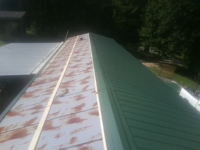 Old rusted panels beside newly installed green metal roofing — Wind Damage Roof Repair by Roofing Brothers in Pine Bluffs
