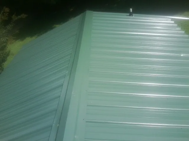 New green metal panels meeting at the ridge of a roof — Flat Roof Repair work by our crew in Pine Bluffs