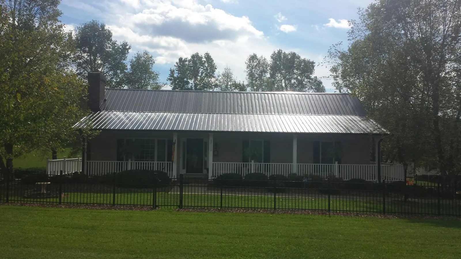 Gray metal roof on a brick ranch with a full width front porch — Gutter Guard Installation work by our crew in Pine Bluffs