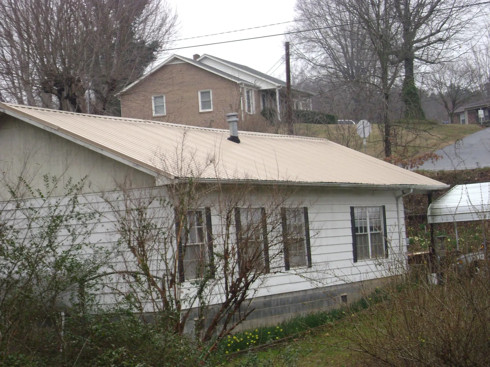 Tan metal roof on a white sided house set into a hillside — Commercial Roofing by Roofing Brothers in Pine Bluffs