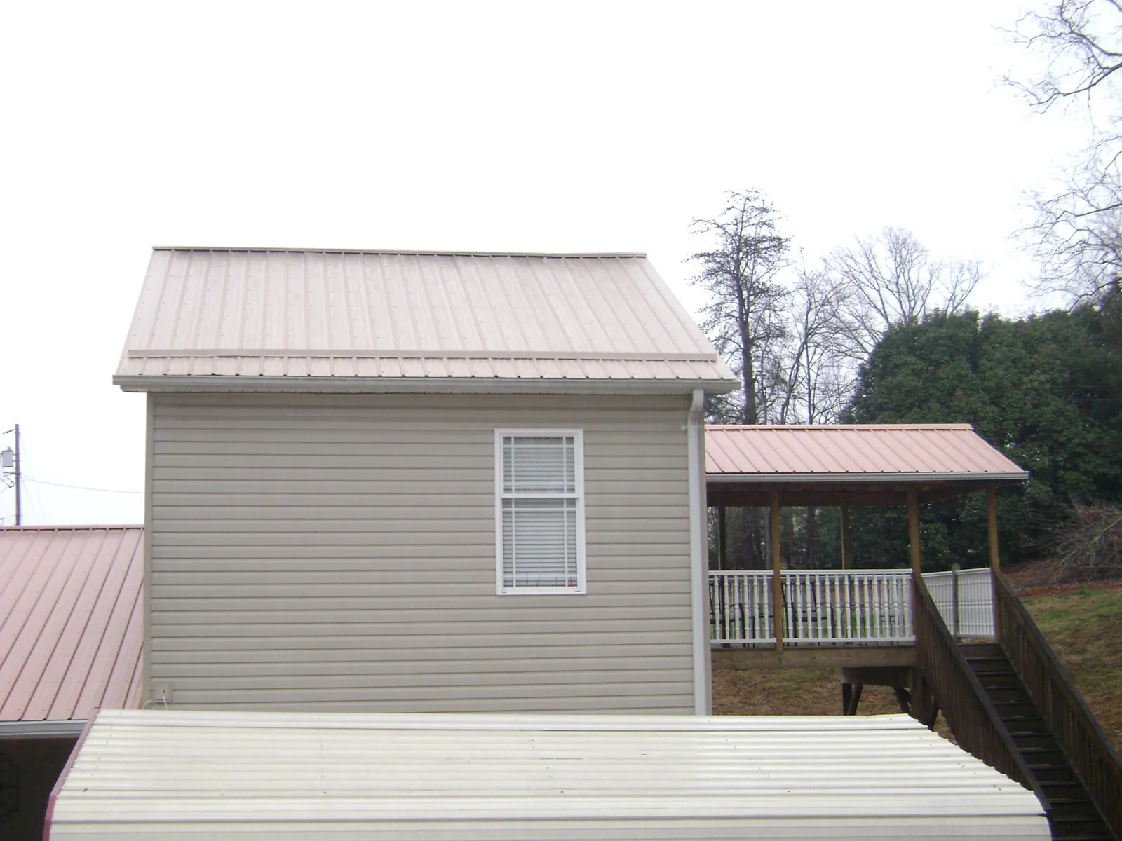 Tan metal roofs on a two story addition and attached porch, from a Roof Replacement job in Pine Bluffs